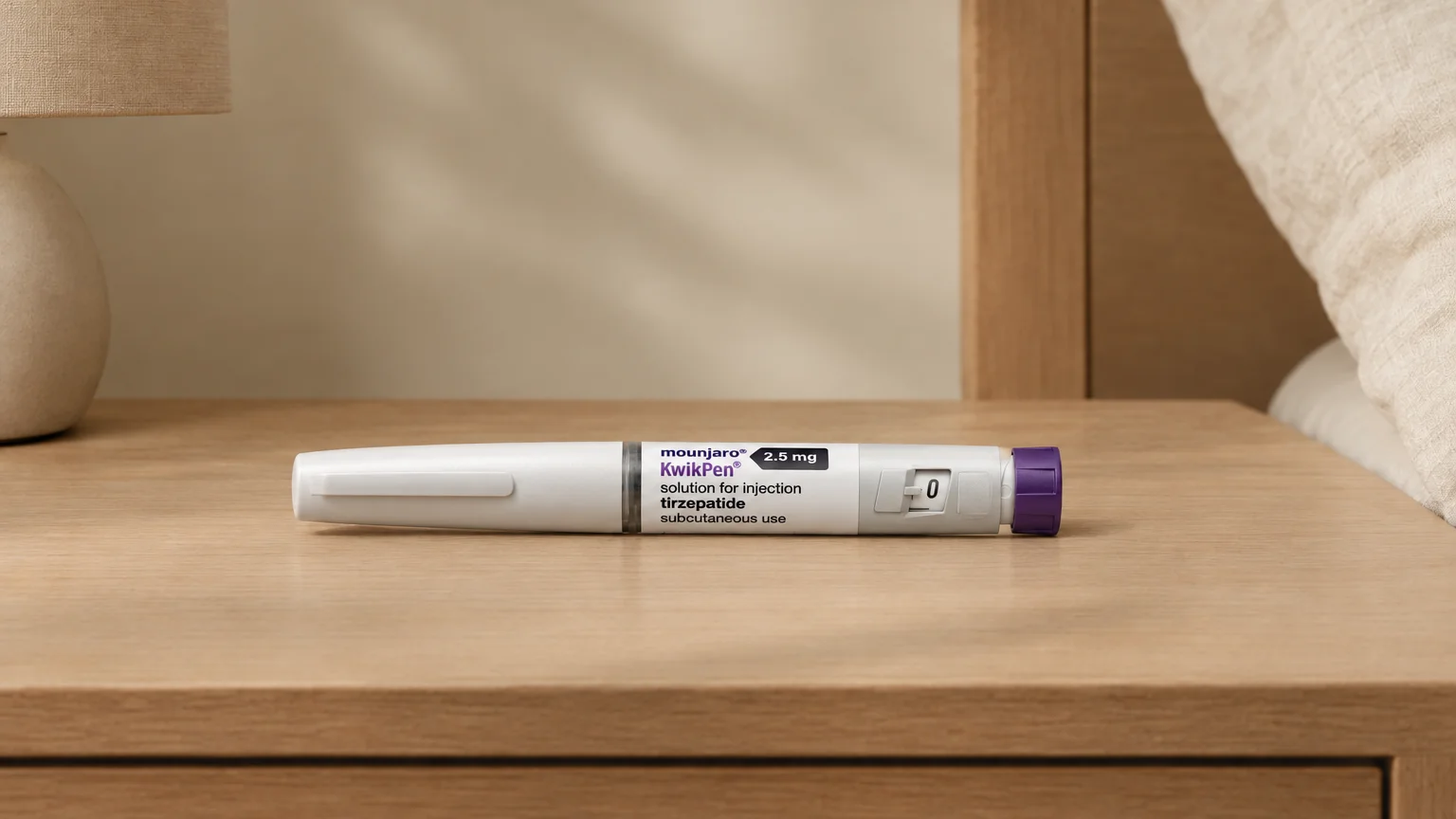 A Mounjaro (tirzepatide) KwikPen lies on a bedside table in warm side light, with cream and pale oak tones and a soft shadow.